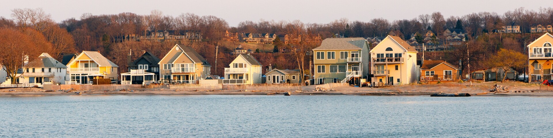 Uma orla marítima com casas ao longo da costa e uma colina arborizada ao fundo.