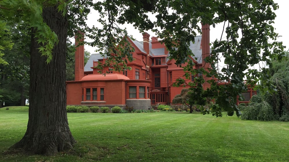 A large, red brick house with a green lawn and trees.