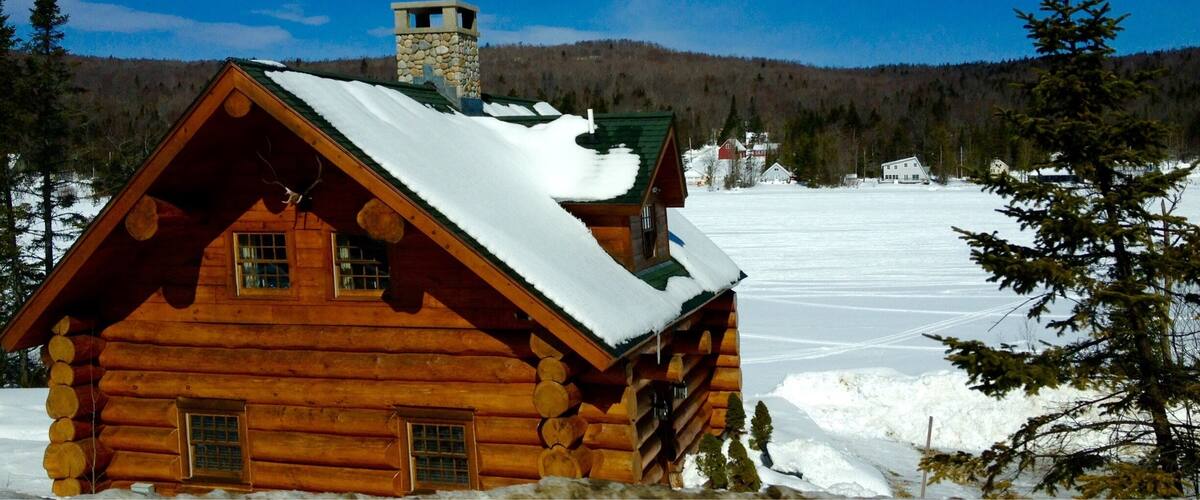 A wooden cabin with a stone tower, surrounded by snow-covered ground and trees.