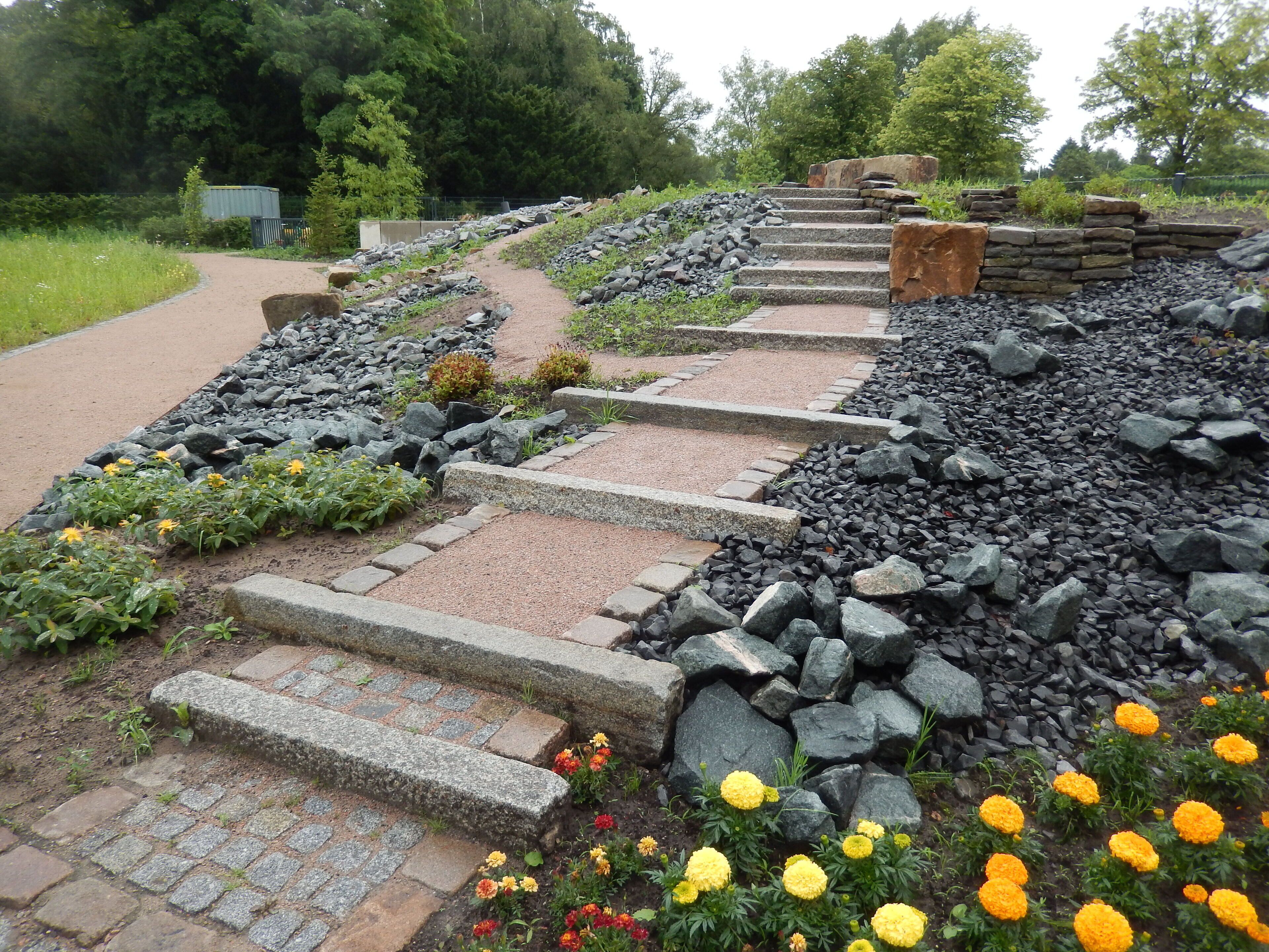 A stone pathway with steps leading up a slope, surrounded by rocks and flowering plants.