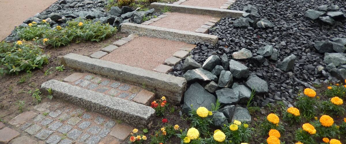 A stone pathway with steps leading up a slope, surrounded by rocks and flowering plants.