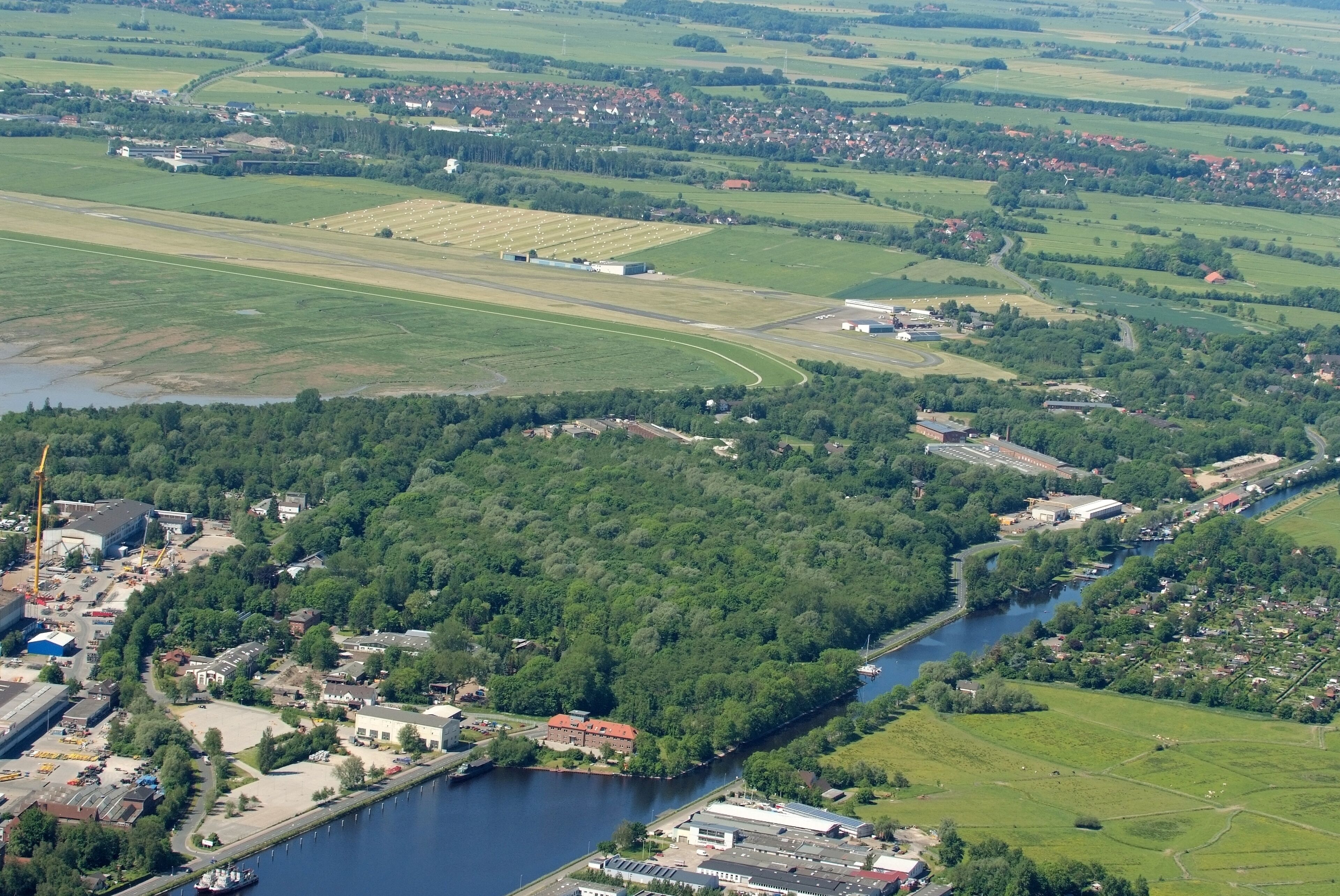 Fotoflug vom Flugplatz Nordholz-Spieka über Cuxhaven und Wilhelmshaven Im Vordergrund der Wilhelmshavener Kanalhafen am Ems-Jade-Kanal, am oberen Bildrand die Gemeinde Sande im Landkreis Friesland, dazwischen der JadeWeserAirport (ehemals Flugplatz Mariensiel).