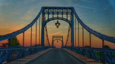 A suspension bridge with a central arch and a street lamp at the top.