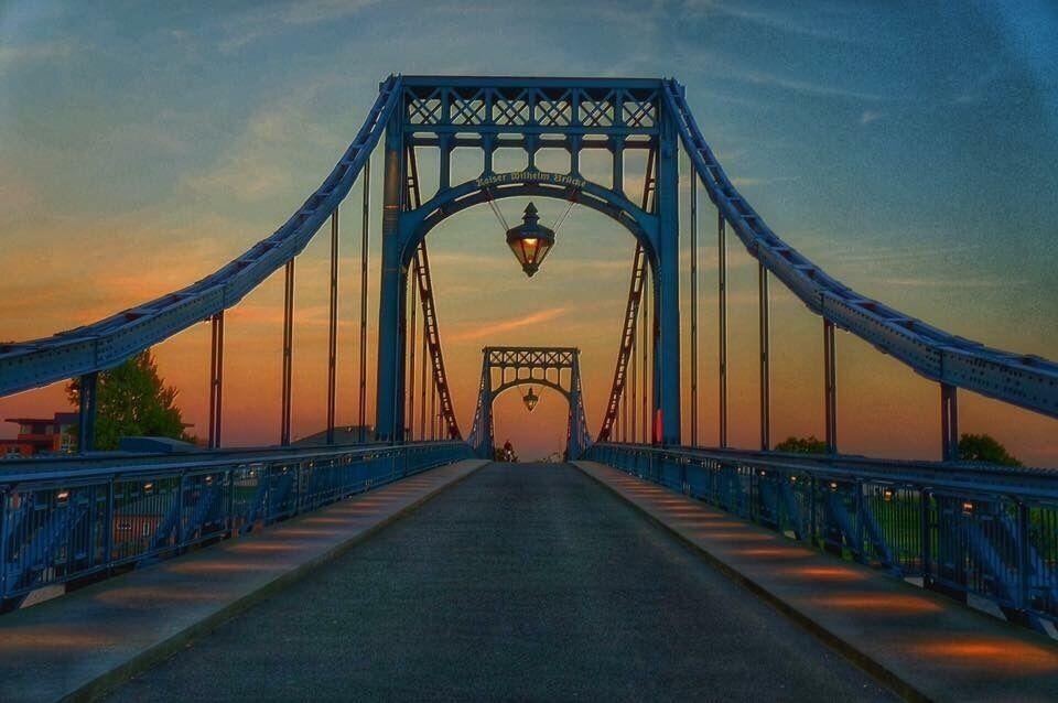 A suspension bridge with a central arch and a street lamp at the top.