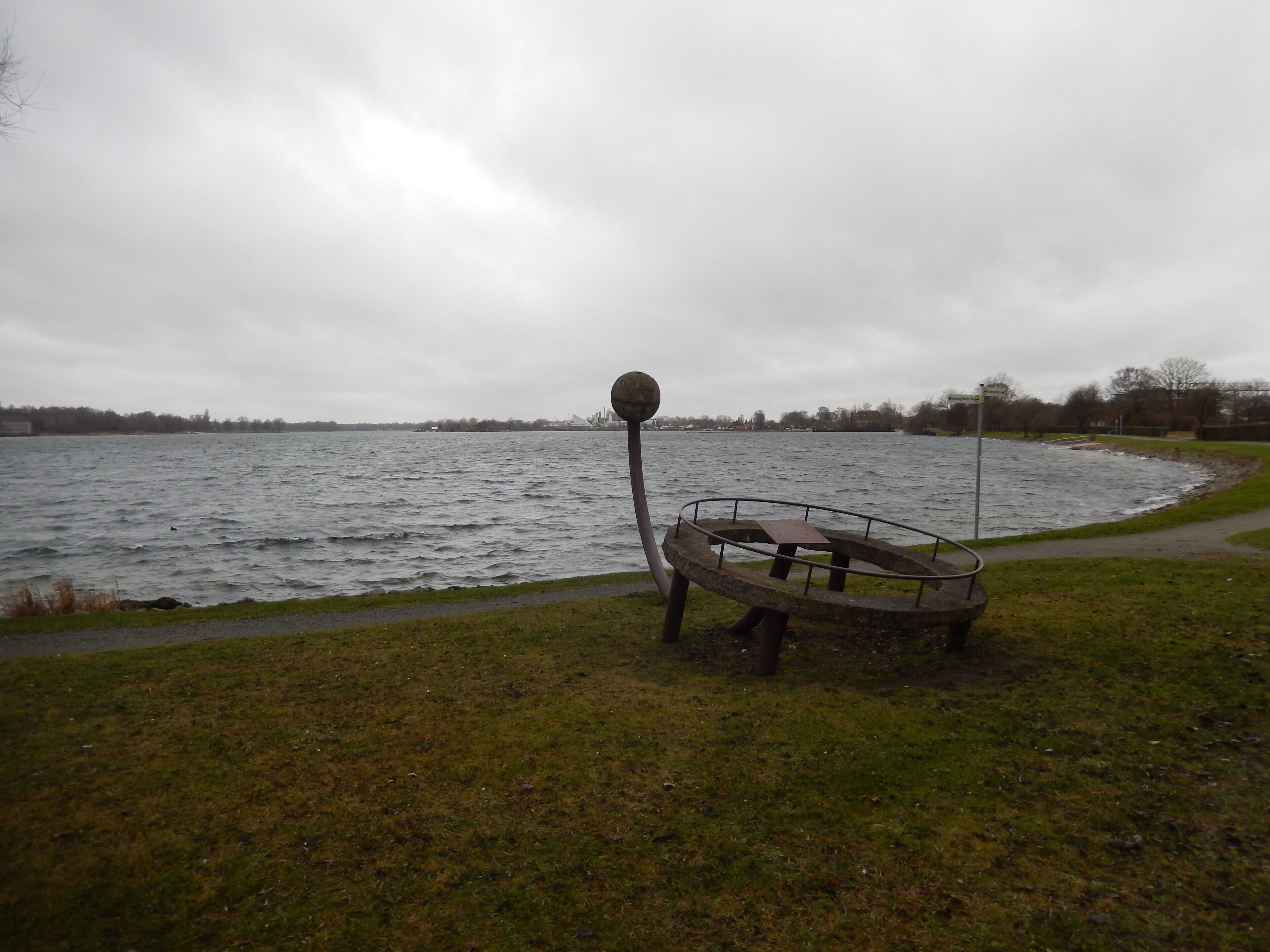 A park with a large body of water, a metal sculpture, and a grassy area.