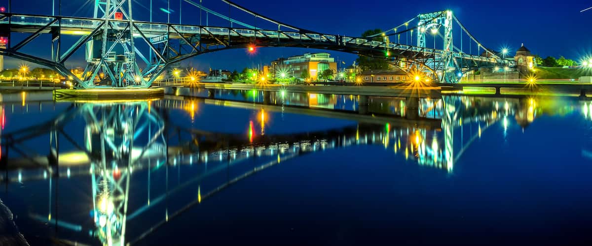 A nighttime view of a bridge with its reflection in the water, illuminated by street lights.