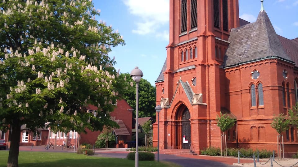 A red brick church with a tall steeple and a large tree with white flowers in front.