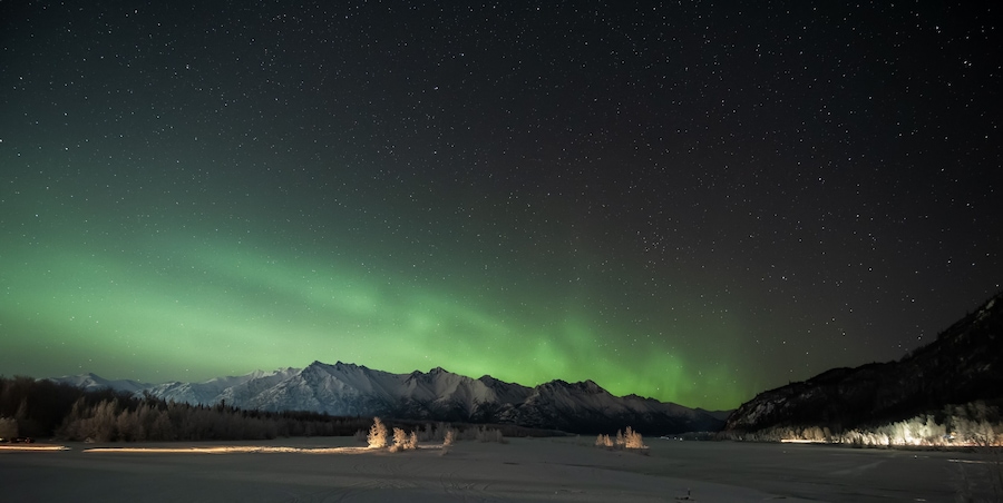 Yötaivas, jonka yllä revontulet tanssivat lumipeitteisten vuorten ja jäätyneen maiseman yllä.