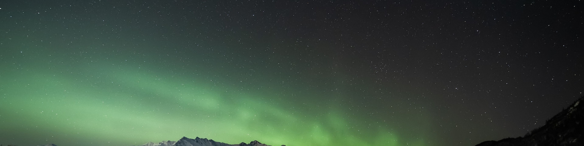 Céu noturno com a aurora boreal sobre montanhas cobertas de neve e uma paisagem congelada.
