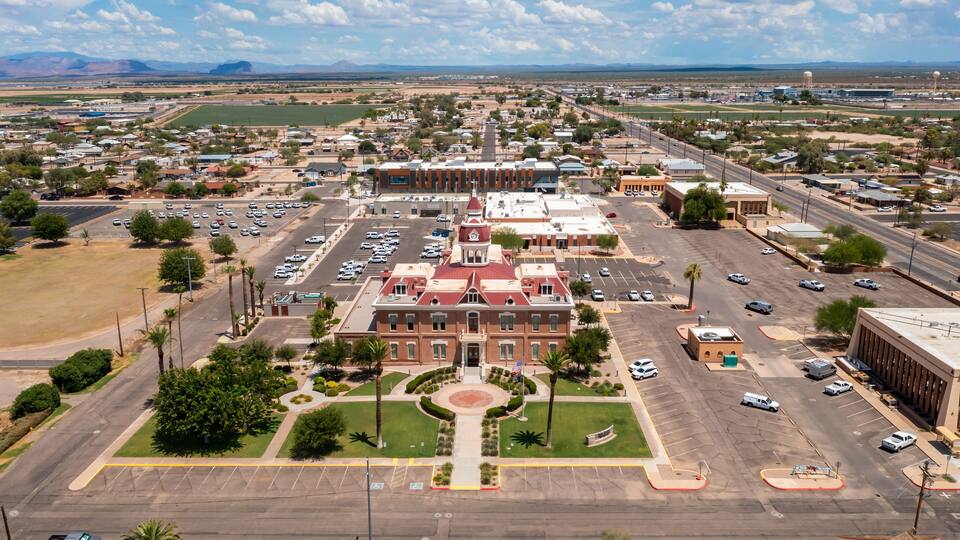 A large, historic building with a red roof and a central courtyard, surrounded by a parking lot and a wide road.