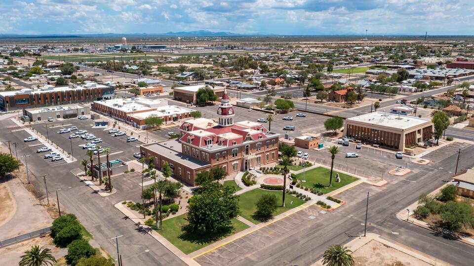 An aerial view of a town with a prominent red-bricked building with a dome, surrounded by streets, parking lots, and greenery.