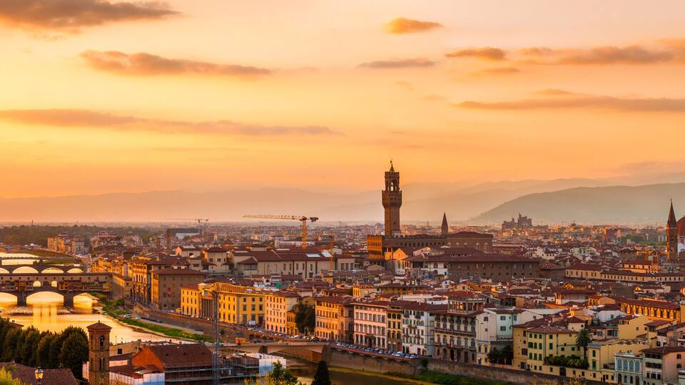 A panoramic view of a city with prominent historical architecture, including a large dome and bell towers, during sunset.