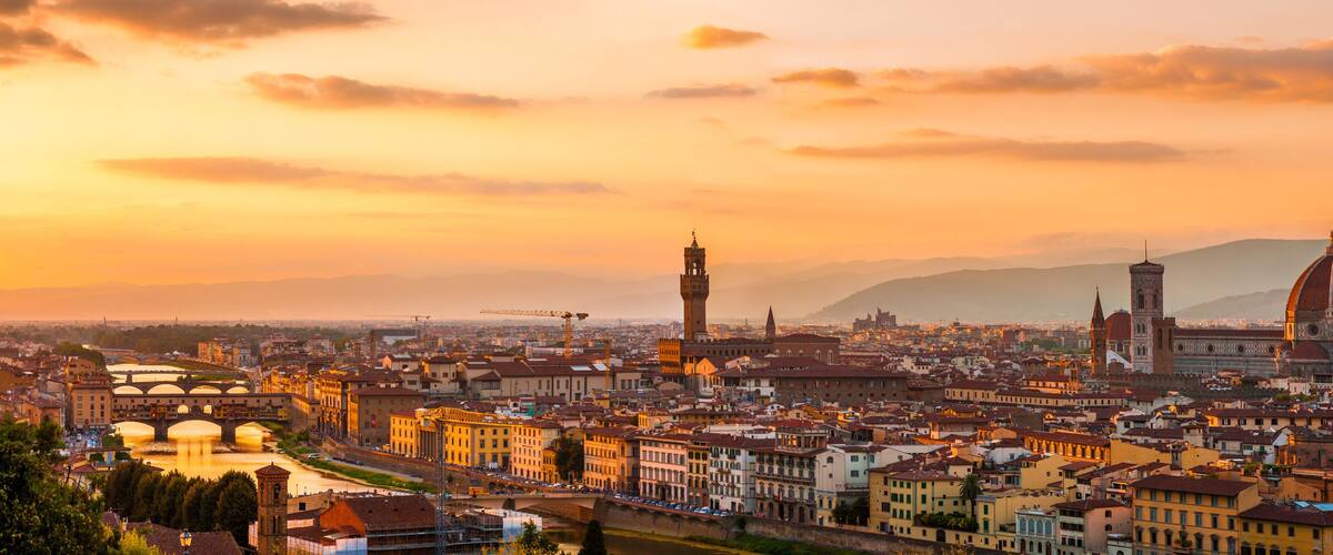 A panoramic view of a city with prominent historical architecture, including a large dome and bell towers, during sunset.