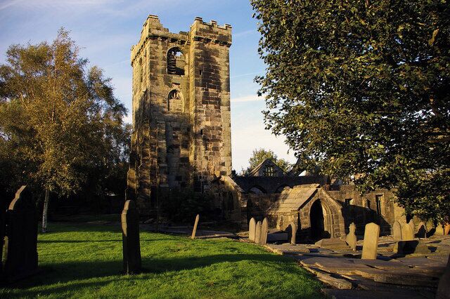 A historic stone tower with arched windows, surrounded by trees and a grassy area with gravestones.