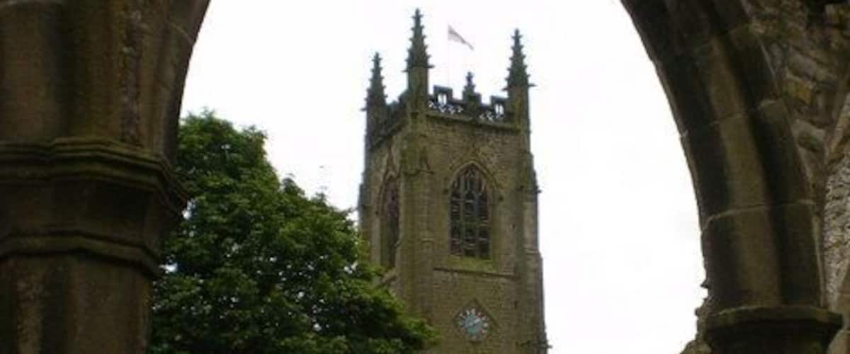 Un antiguo arco de piedra enmarca la torre histórica de una iglesia con un reloj.