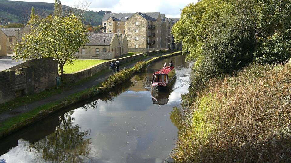 A narrow canal with a red boat, stone buildings, and greenery along the banks.