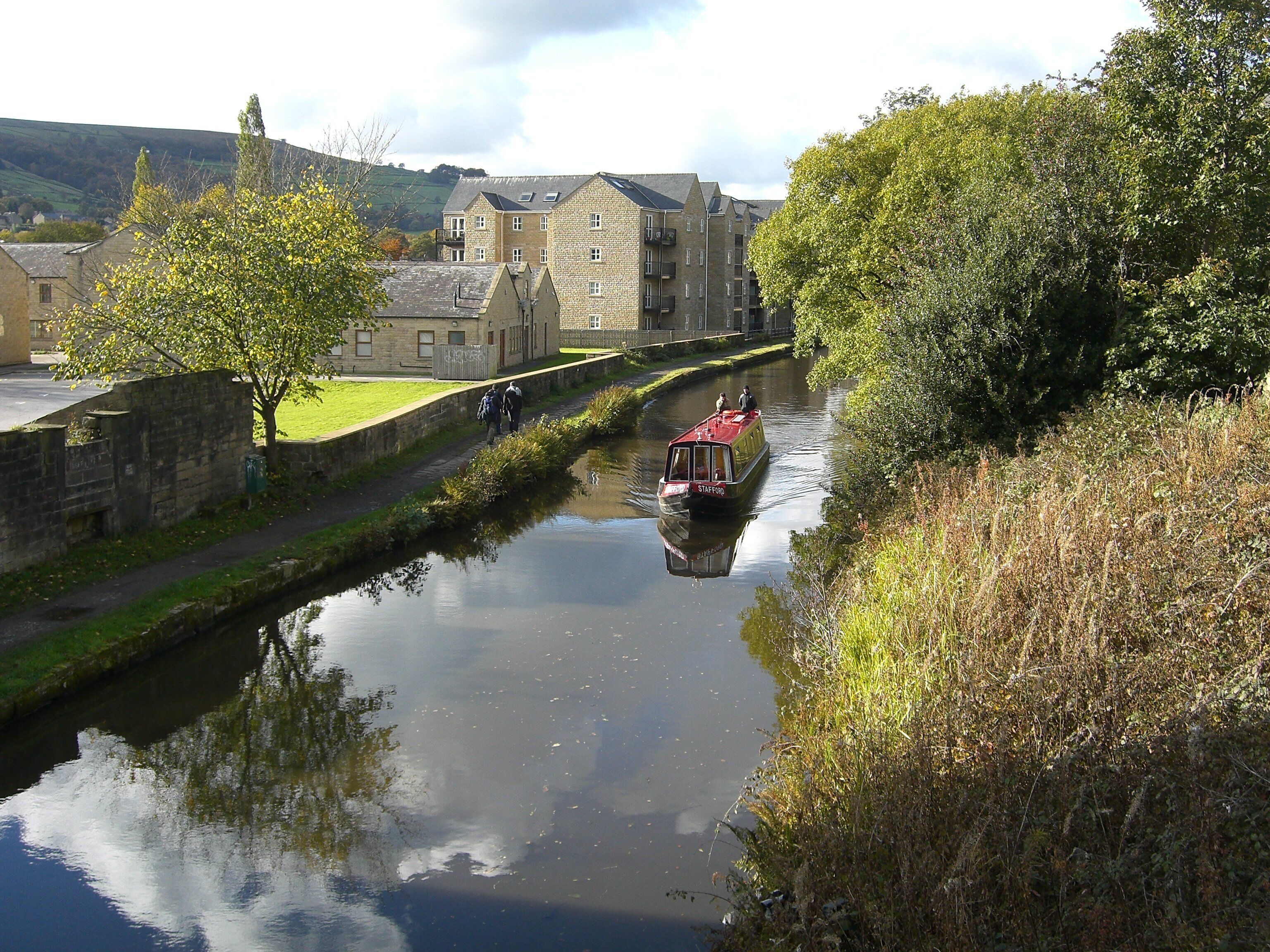 A narrow canal with a red boat, stone buildings, and greenery along the banks.