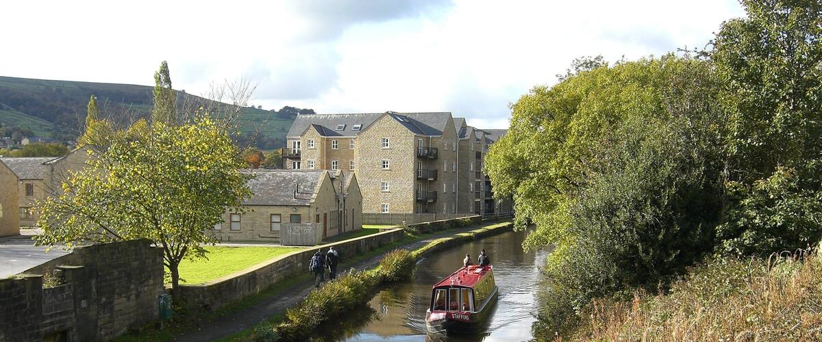 A narrow canal with a red boat, stone buildings, and greenery along the banks.