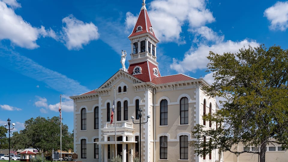 A historic courthouse with a prominent clock tower, surrounded by a well-maintained lawn and a clear blue sky.