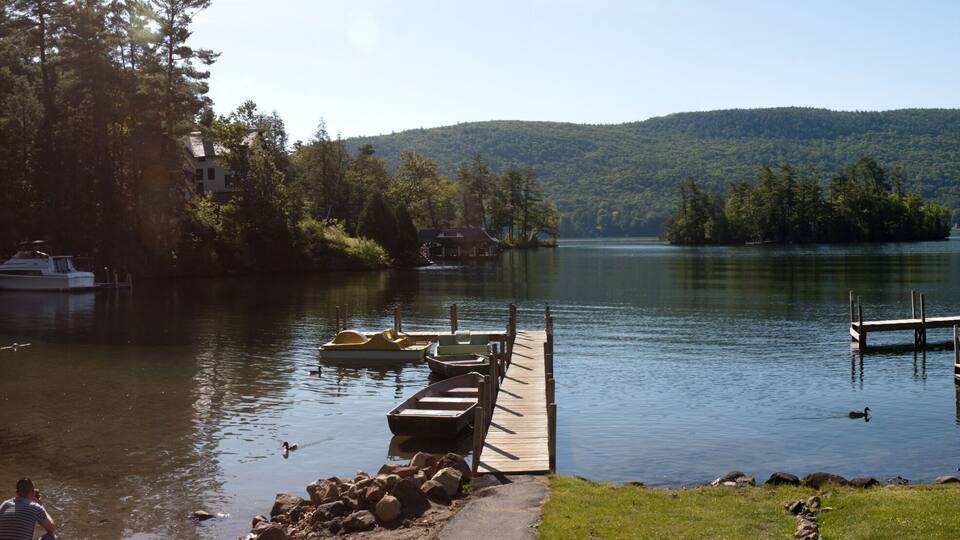 A lake with boats docked at a pier, surrounded by lush greenery and hills.