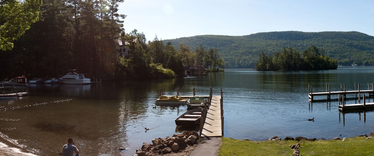 A lake with boats docked at a pier, surrounded by lush greenery and hills.