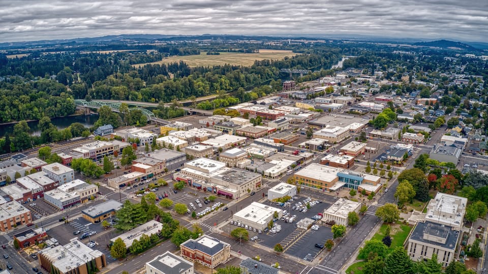 An aerial view of a town with a river, green spaces, and a bridge.