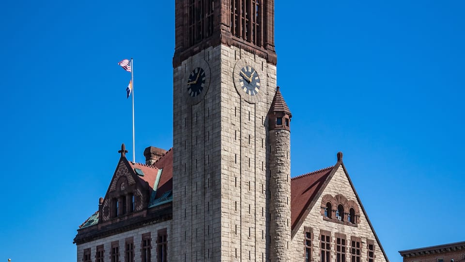 A historic building with a clock tower, arched windows, and a flagpole.