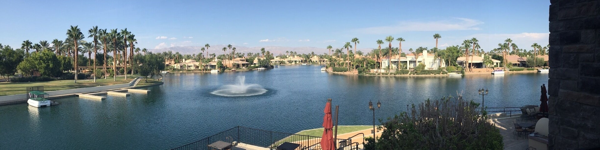 A lake with a fountain, surrounded by palm trees and buildings.
