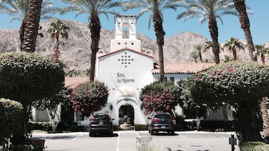 A white building with a bell tower labeled "SPA LA QUINTA" surrounded by palm trees and a mountainous backdrop.