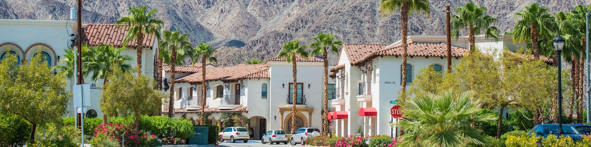A residential area with white buildings, palm trees, and mountains in the background.