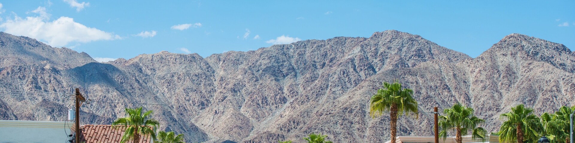 A residential area with white buildings, palm trees, and mountains in the background.