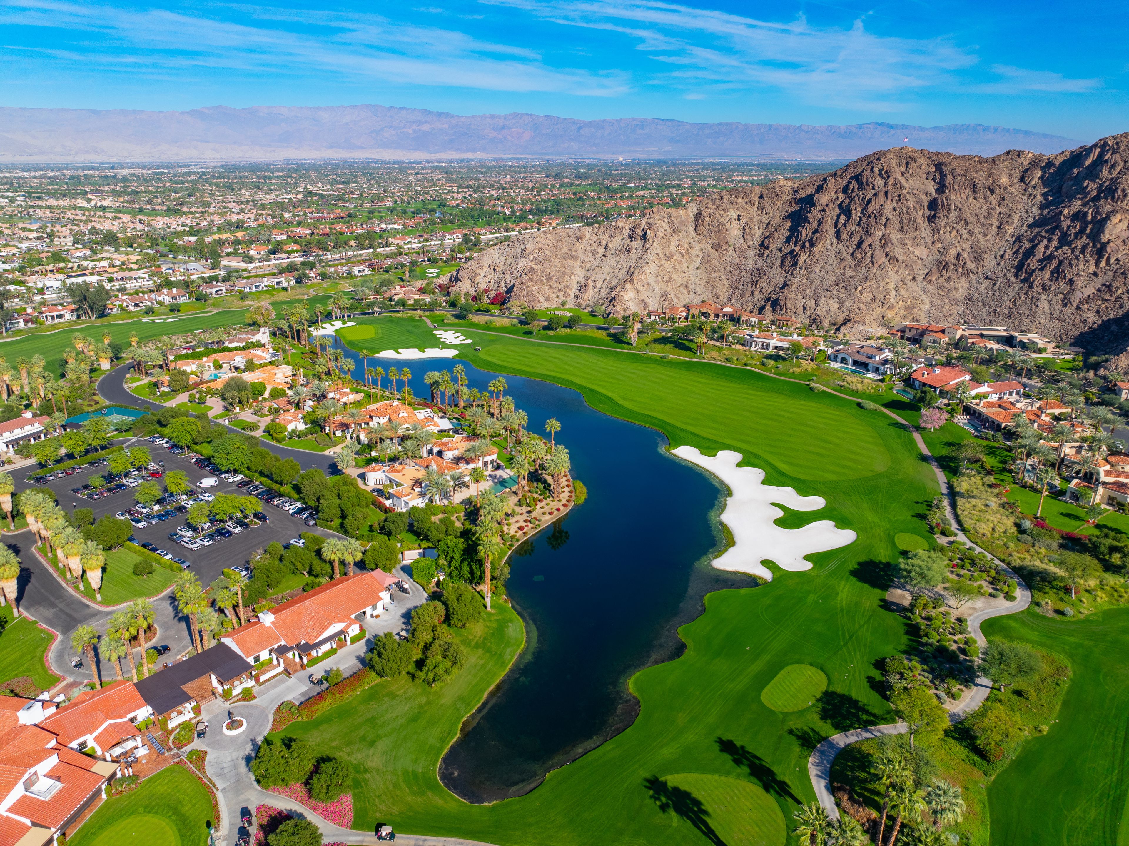 A golf course with a lake, surrounded by residential areas and mountains.