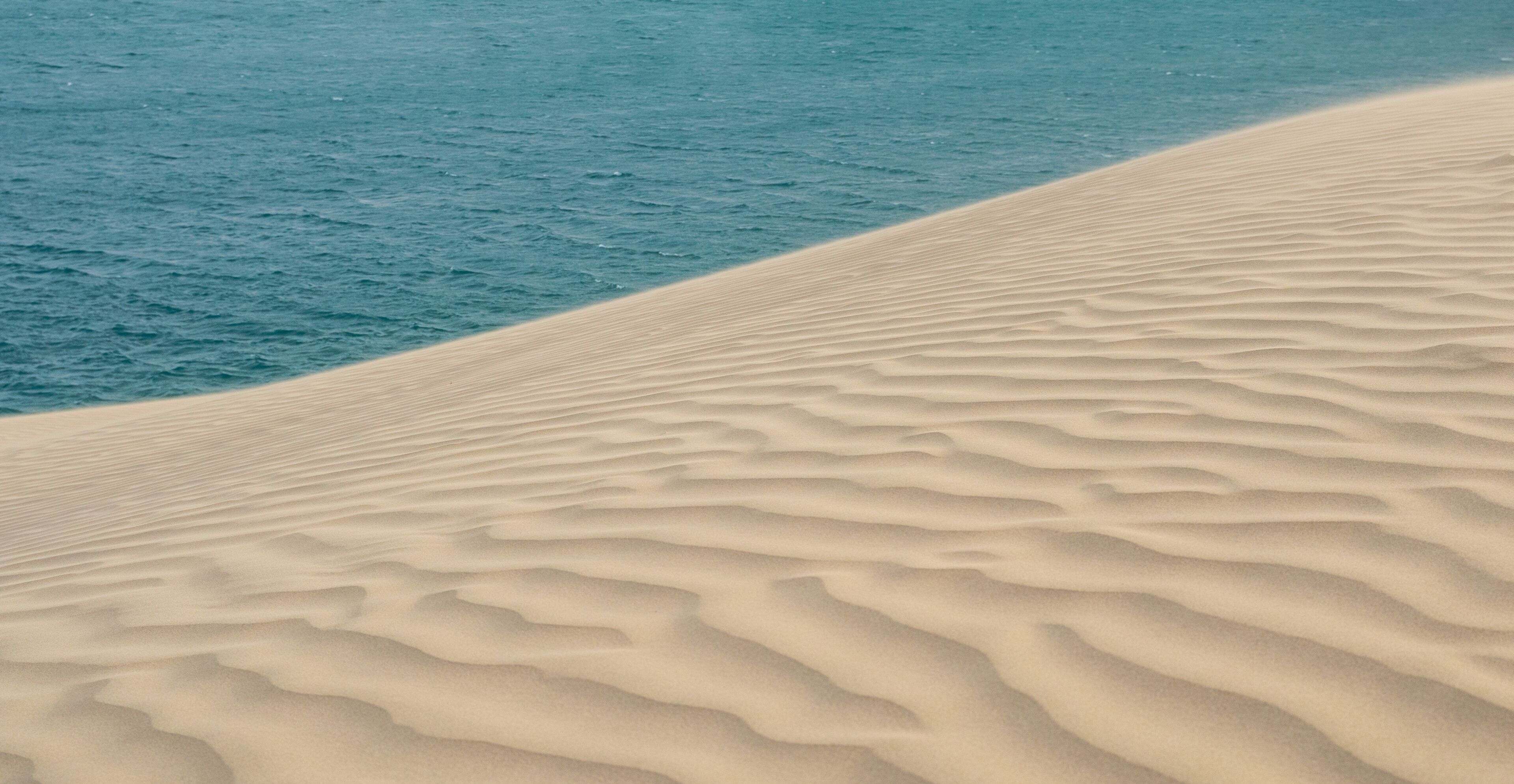 A sandy beach with rippled patterns and a calm blue ocean.