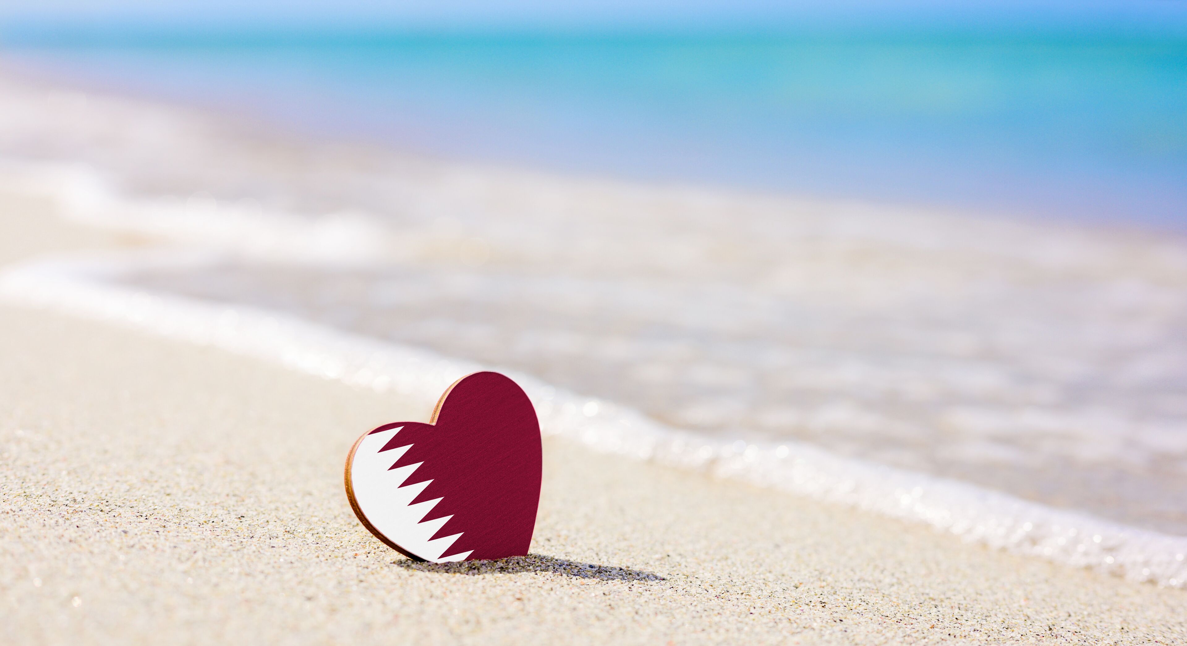 A heart-shaped object on a sandy beach with ocean waves in the background.