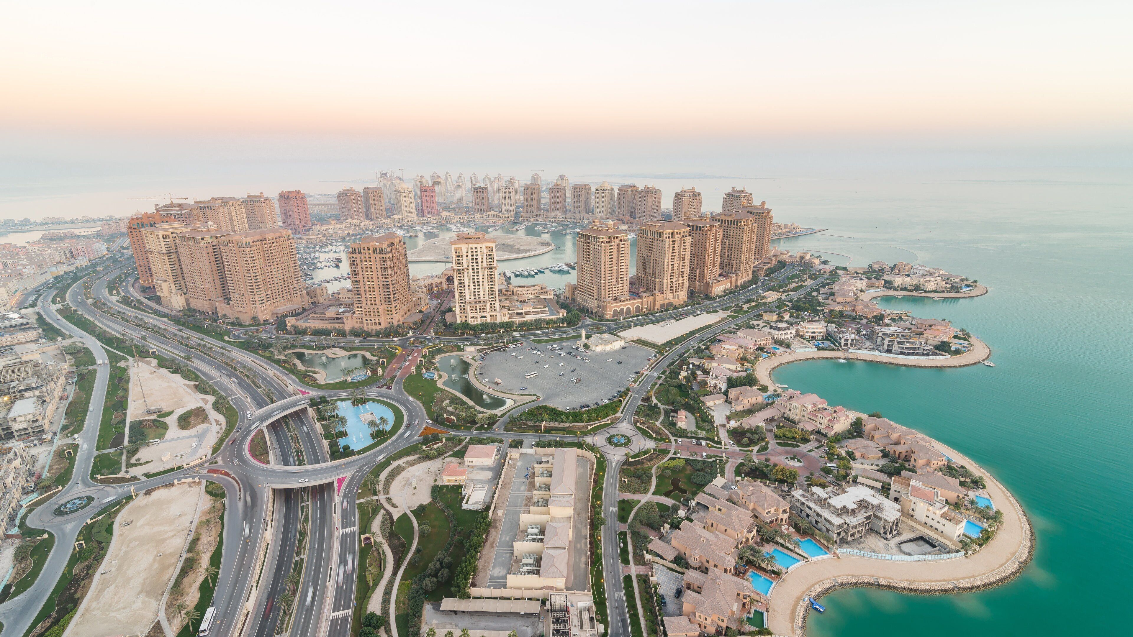 A coastal cityscape with high-rise buildings, a marina, and a roundabout.
