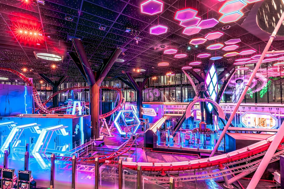 A brightly lit indoor amusement park with roller coasters and neon lights.