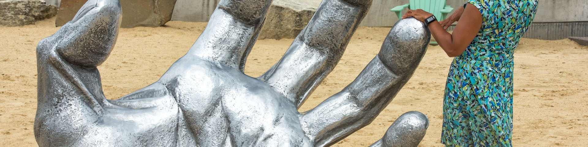 Una gran escultura de mano metálica en una zona arenosa con una persona de pie cerca.