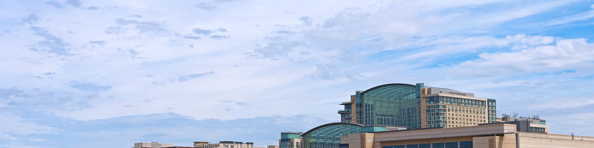 National Harbor waterfront panorama in Oxon Hill, Maryland, USA. Sun shines through cumulus clouds on National Harbor pier and modern buildings along coastline of Potomac River.