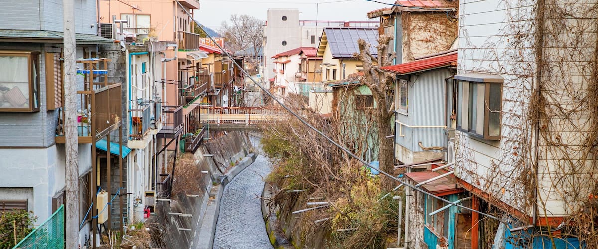 A narrow alley flanked by multi-story buildings with visible balconies and a small water channel running through the center.