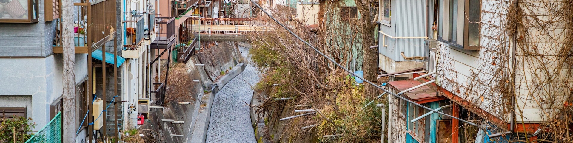 A narrow alley flanked by multi-story buildings with visible balconies and a small water channel running through the center.