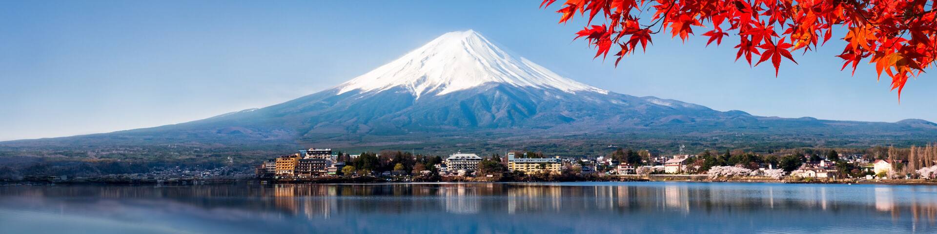 A snow-capped mountain, a calm lake, and buildings along the shore.