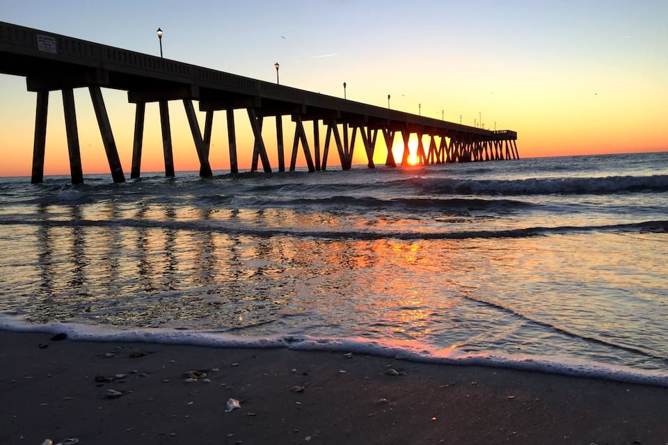 Un muelle se adentra en el océano al atardecer, con el sol ocultándose en el horizonte.