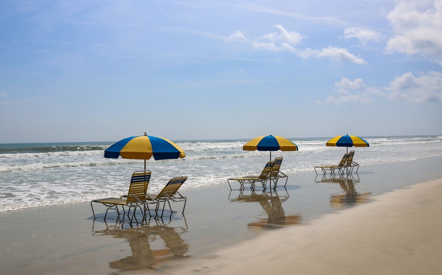 Una playa con tres sombrillas y sillas de playa.