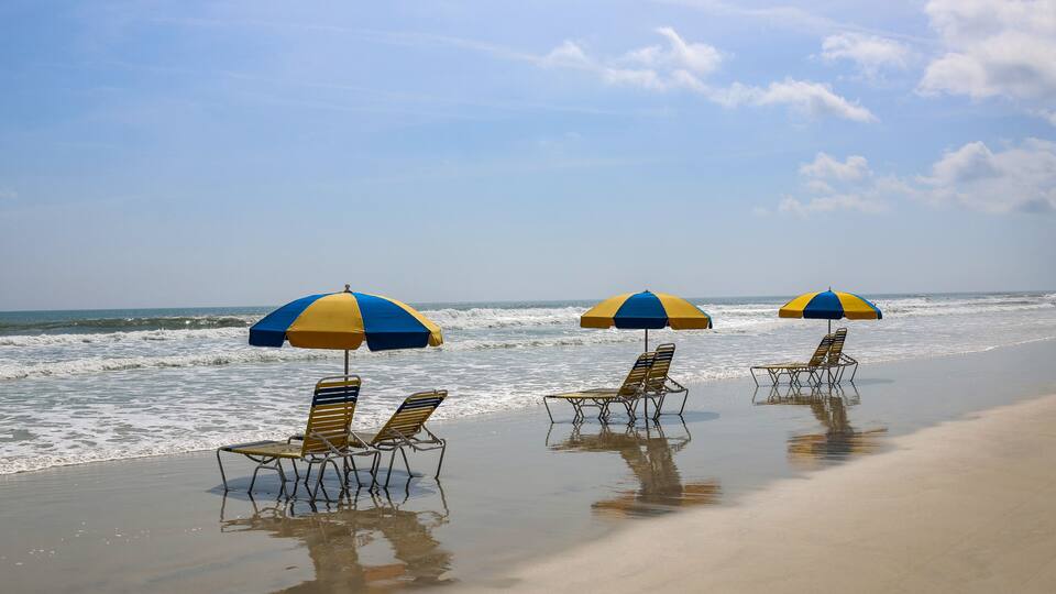 A beach with three umbrellas and lounge chairs.