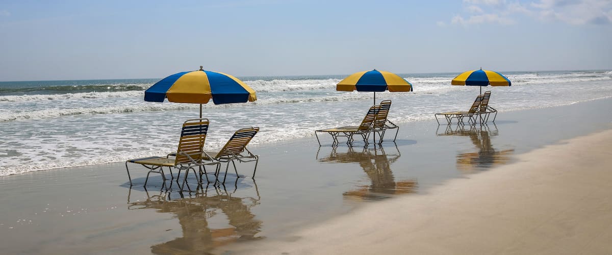 A beach with three umbrellas and lounge chairs.