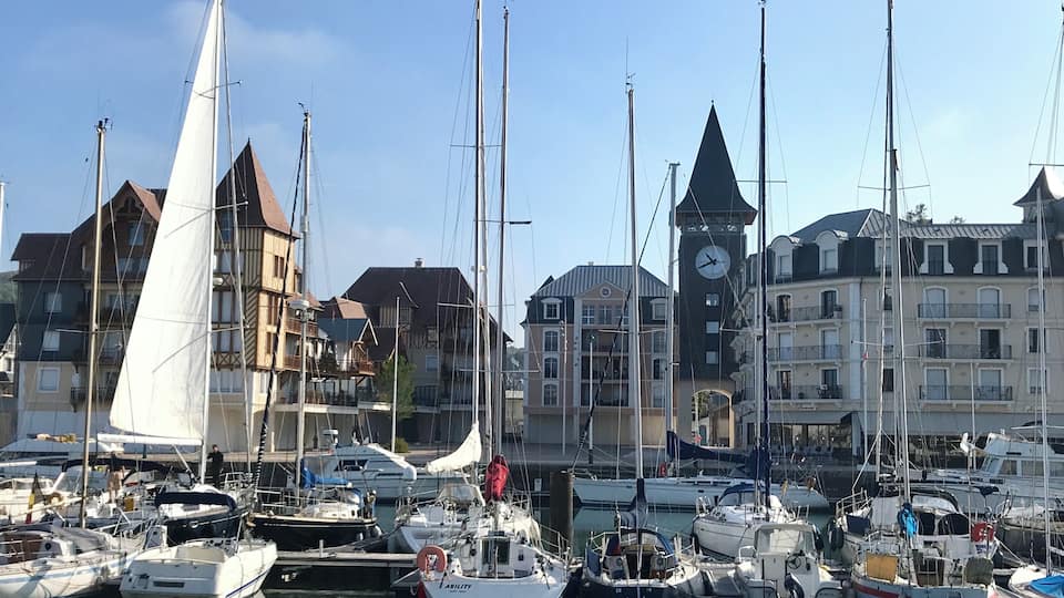 A marina with sailboats docked, surrounded by historic buildings and a clock tower.