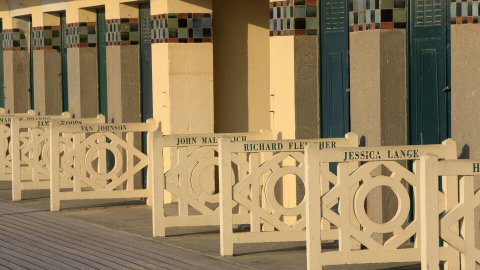 A row of white wooden gates with names on them, leading to a building with colorful tiled walls.