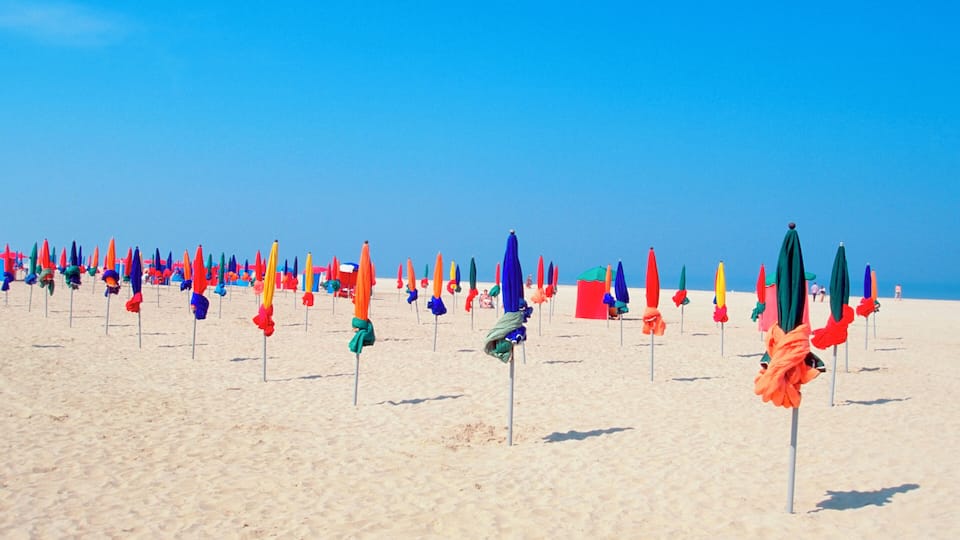 A beach with colorful umbrellas and a clear blue sky.