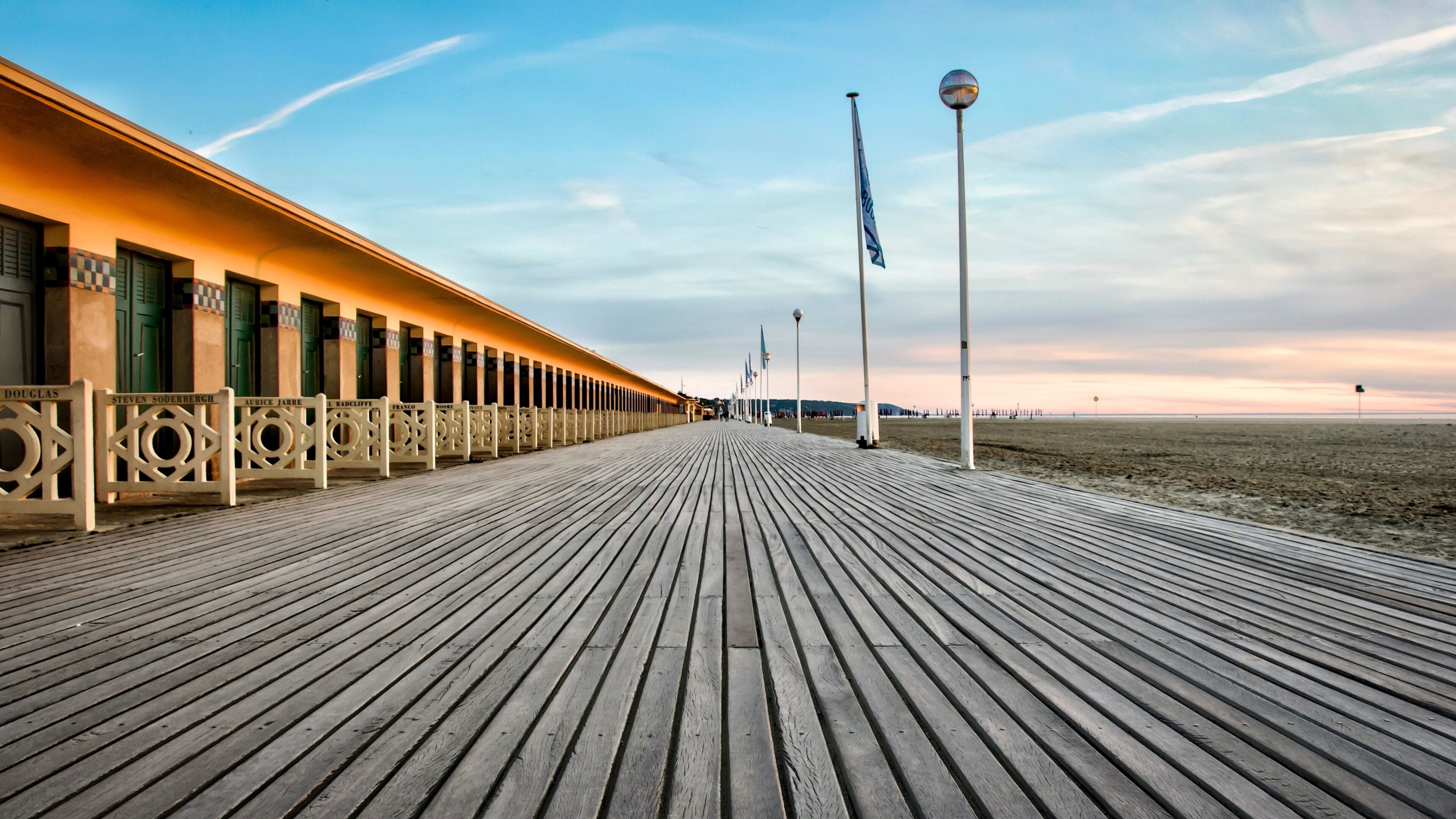 A wooden boardwalk leading to beachside buildings with flags.