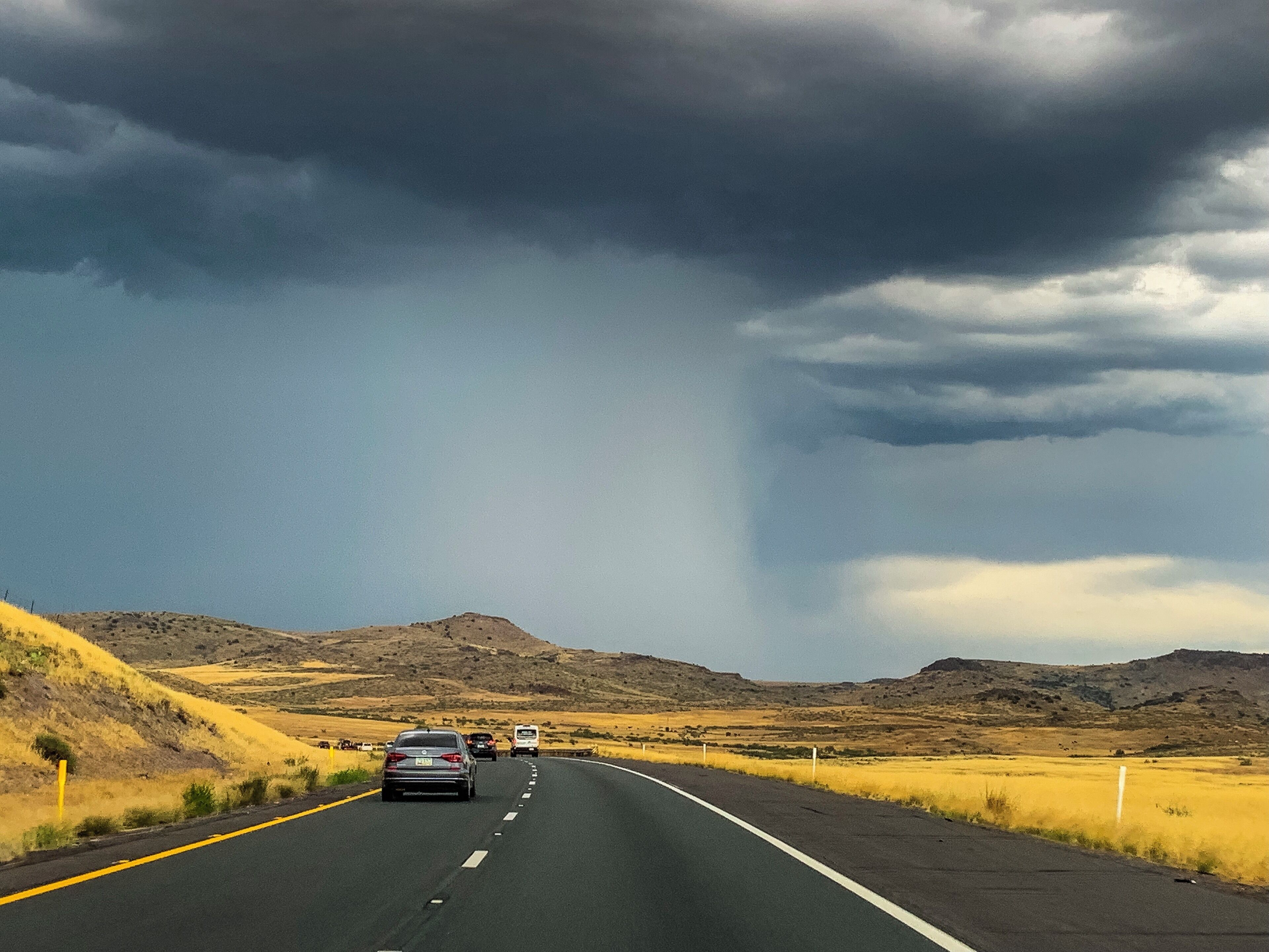 A highway with cars, surrounded by dry grasslands and hills under a stormy sky.